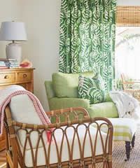 Rattan chair with red blanket, green patterned curtains, and a lamp in a bright room.