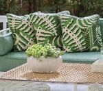 Three green and white leaf-patterned pillows on a light blue outdoor couch with a small white succulent pot.