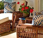 Wicker outdoor furniture with blue patterned pillows and potted red geraniums.