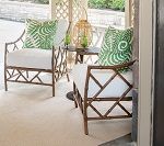 Two bamboo-style chairs with white cushions and green leaf pillows on a porch.