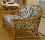 Wicker loveseat with blue patterned cushions, next to a small side table.