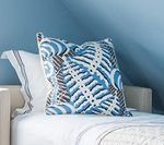 Blue patterned pillow on a white bed with a light blue wall in the background.