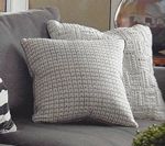 Two textured gray square pillows on a gray couch.