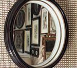 Round mirror reflecting framed artwork on a textured wall.