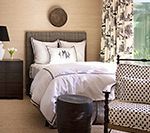 Bedroom with neutral walls, bed with white bedding, patterned curtains, and a patterned chair.