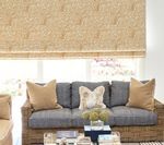 Beige woven shade above a blue-cushioned sofa with gold pillows, coffee table with decor.