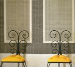 Two ornate black chairs with yellow seats in front of textured gray wallpaper with two white-framed panels.