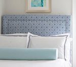 Blue patterned headboard with white bedding and light blue bolster pillow.