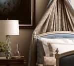 Bedroom with draped canopy bed, crystal lamp on nightstand, framed artwork.