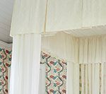 Cream canopy bed with sheer curtains and patterned wallpaper in a bedroom.