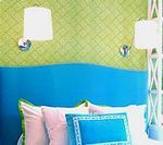 Blue headboard with pink and blue pillows, green patterned wall, and sconce lights.