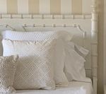 White bed with pillows against a striped beige and white wall; headboard resembles bamboo.