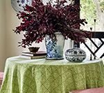 Round table with a green tablecloth, vase of burgundy branches, and decorative objects.