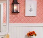 Bathroom with coral patterned wallpaper, black lantern, framed art, and white wainscoting.