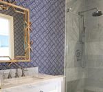 Bathroom with blue patterned wallpaper, gold mirror, marble countertop and shower.