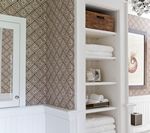 Built-in white shelves with folded white towels and a brown wooden box. Damask wallpaper and white cabinetry in a bathroom.