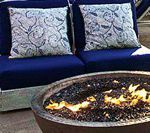 Blue outdoor seating with decorative pillows, near a lit fire pit.