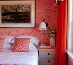 Bedroom with red patterned wallpaper, white bedding, and a black and white artwork.
