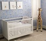 White crib in a nursery with blue patterned walls, framed art, and a stuffed giraffe.