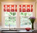 Two windows with red patterned roman shades above a kitchen sink, with a vase of purple flowers and a red bowl.