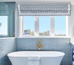 Blue bathroom with a white tub under a window with a patterned shade.