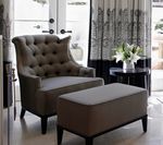Gray tufted armchair and ottoman with dark wood legs; flowers on a side table.