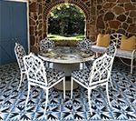 Outdoor patio with white furniture, patterned blue tile floor, and stone wall backdrop.