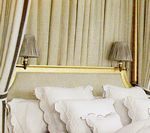 Bed with white bedding and gray lamps, cream-colored curtains in a room.