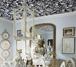 Ornate dining room with floral ceiling wallpaper, chandelier, and a large mirror.