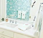 White bathroom sink with towels and floral wallpaper reflected in the mirror.