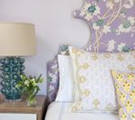 Bedroom with floral headboard, teal lamp, and decorative pillows.