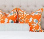 Two orange floral pillows and a light blue bolster pillow on a bed.