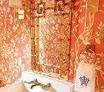 Coral floral wallpaper bedroom with gold-framed mirror and sconces. White bed with decorative pillow.