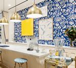 A brightly lit cafe with blue floral wallpaper, a yellow square, and brass pendant lights.