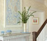 Hallway with artwork, white console table, vase with greenery, and a staircase.