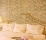 Bedroom with white bedding, headboard, and floral wallpaper.