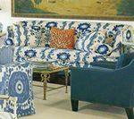 Blue patterned sofa with accent pillows, blue armchair, and a small gold table.