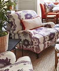 Upholstered armchair with purple and white floral pattern, a red pillow, and a wicker plant pot.
