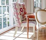 Dining chair with floral print back by a sunny window.