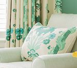 Cream armchair with floral patterned pillow and curtains in teal and white.