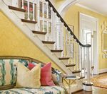 Yellow hallway with a staircase, floral bench, and colorful pillows.