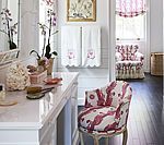 Elegant bathroom with white vanity, floral chair, and pink accents.