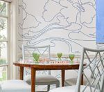 Dining room with round wooden table, white chairs, floral wallpaper, and green glasses.