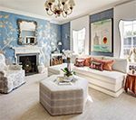 Living room with blue floral wallpaper, white sofa, fireplace, and octagon-shaped ottoman.