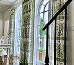 Two arched windows with patterned green and white curtains, staircase in foreground.
