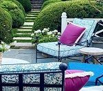 Outdoor seating area with blue patterned cushions, purple pillows, and lush green hedges.