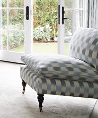 Blue and gray patterned chaise lounge with a pillow, in front of a window.