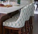Three patterned upholstered bar stools at a marble-topped kitchen island with food.