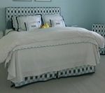 Bed with patterned headboard, white bedding with blue trim, and matching bed skirt.