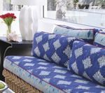 Blue patterned cushions on a woven sofa near a window with a vase and decor.